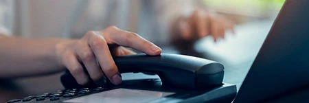 Person holding telephone down on desk