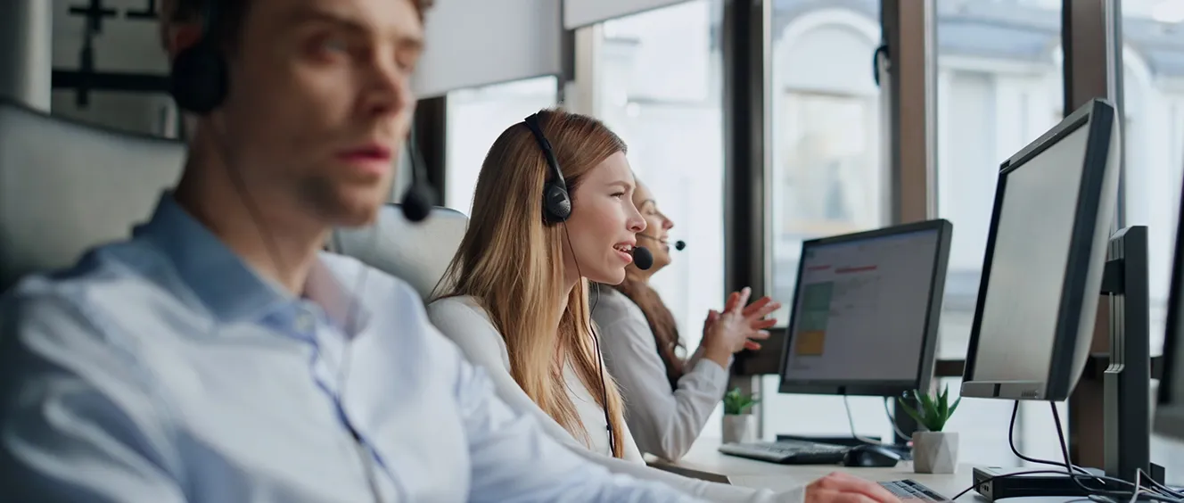 People talking with headsets on while looking at computer monitors
