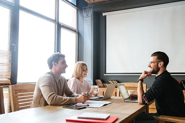 Three people in a meeting room with laptops