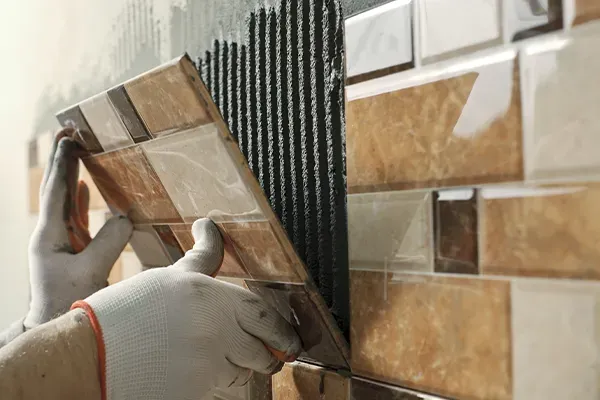 Person placing tiles on wall with gloves
