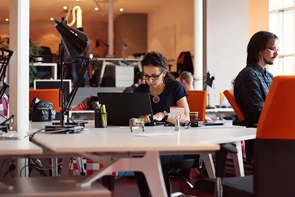 Woman with glasses looking down at laptop on desk