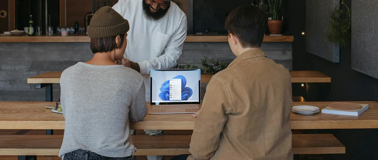 Two people sitting down looking at laptop while man looks over